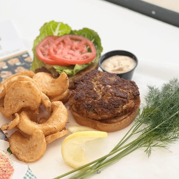 Chefhouse crab cake sandwich with lettuce, tomato, curly fries, sauce, lemon, and dill.