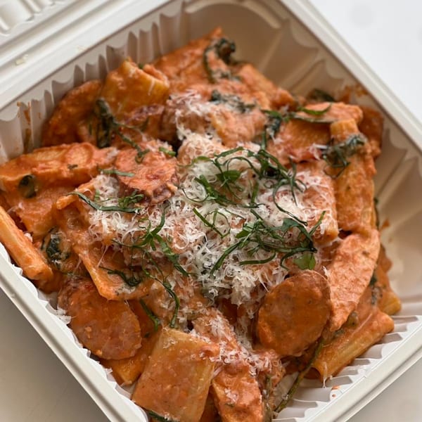 Chefhouse's creamy pasta with red sauce, grated cheese, and fresh herbs in a takeout container.