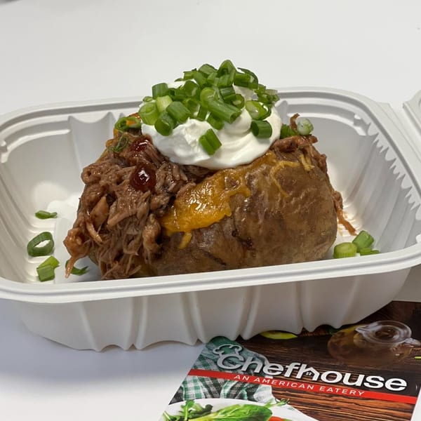 Chefhouse baked potato with pulled pork, cheese, sour cream, and green onions in a takeout container.