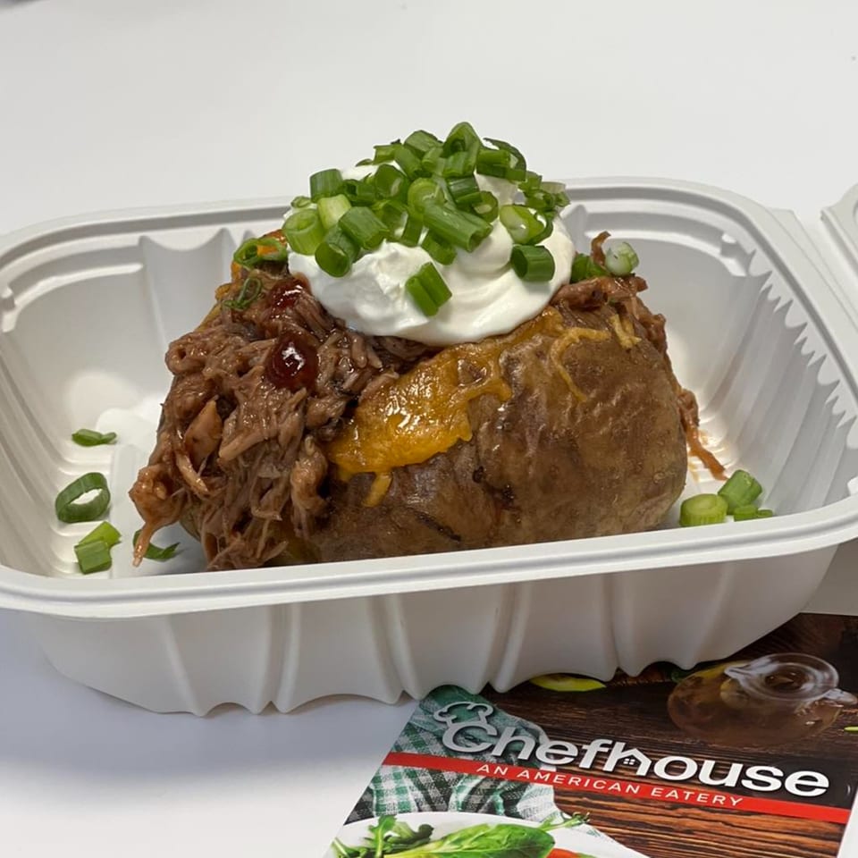 Chefhouse baked potato with pulled pork, cheese, sour cream, and green onions in a takeout container.