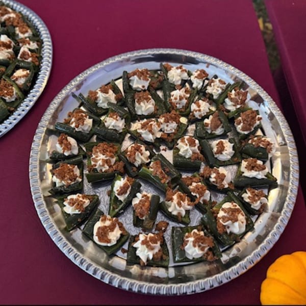 A silver platter filled with green appetizers topped with white cream and brown crumbles.