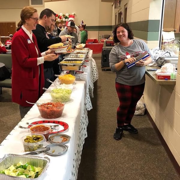 People serving themselves from a buffet line with various American dishes and toppings.