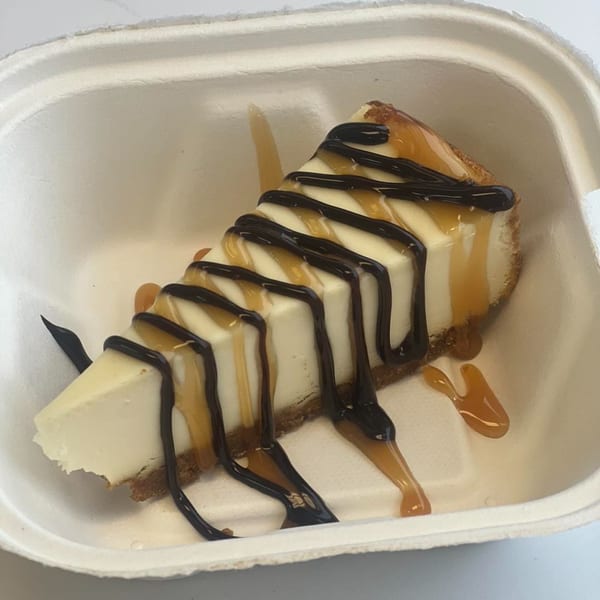 Chefhouse cheesecake slice with chocolate and caramel drizzle in a white takeout container.
