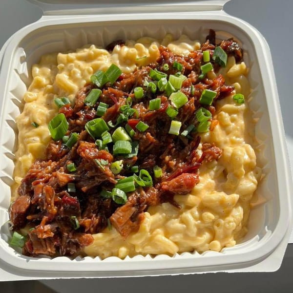 Chefhouse's mac and cheese topped with barbecue pulled pork and chopped green onions in a takeout container.